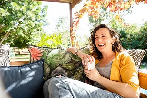 Vrouw zit lachend in haar tuin te ontspannen met een koffie