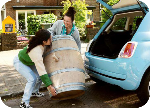 Vrouwen tillen houten wijnvat uit blauwe auto