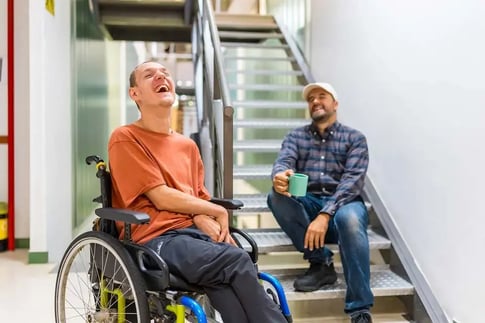 Man in rolstoel lacht samen met begeleider
